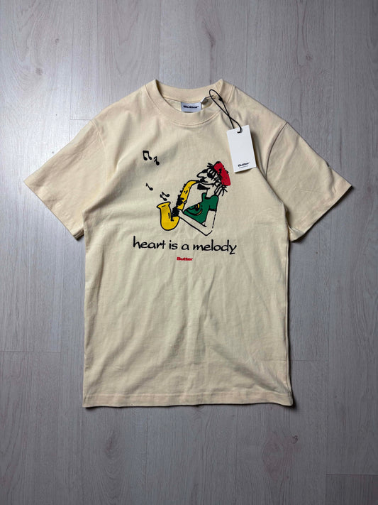 Beige Butter T-shirt “Heart Is a Melody” in maat Small, voorkant met tekstprint, nieuw met tags, verkrijgbaar bij Redressed.

